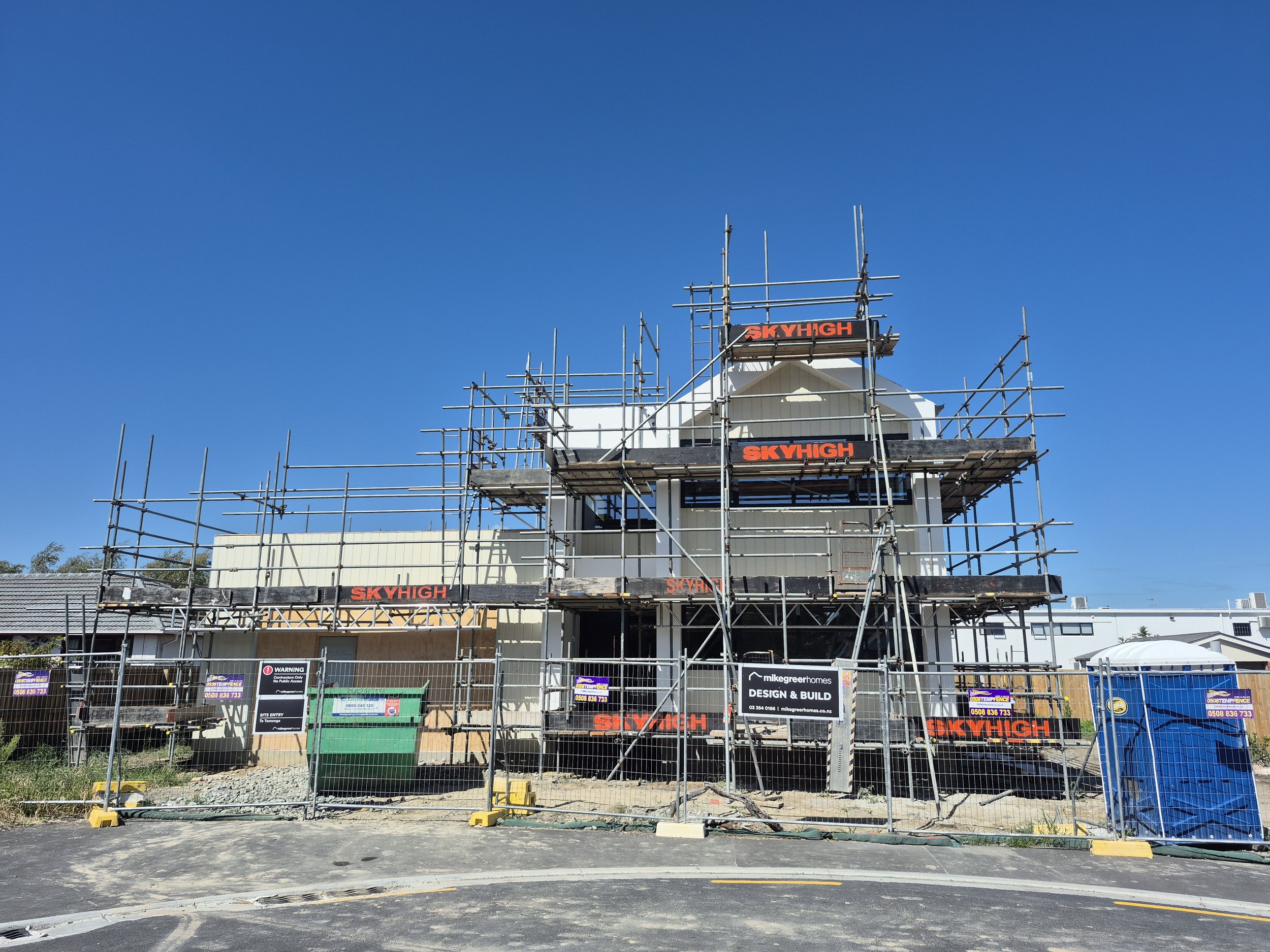 Construction site with scaffolding surrounding a building under renovation, with a clear blue sky overhead.