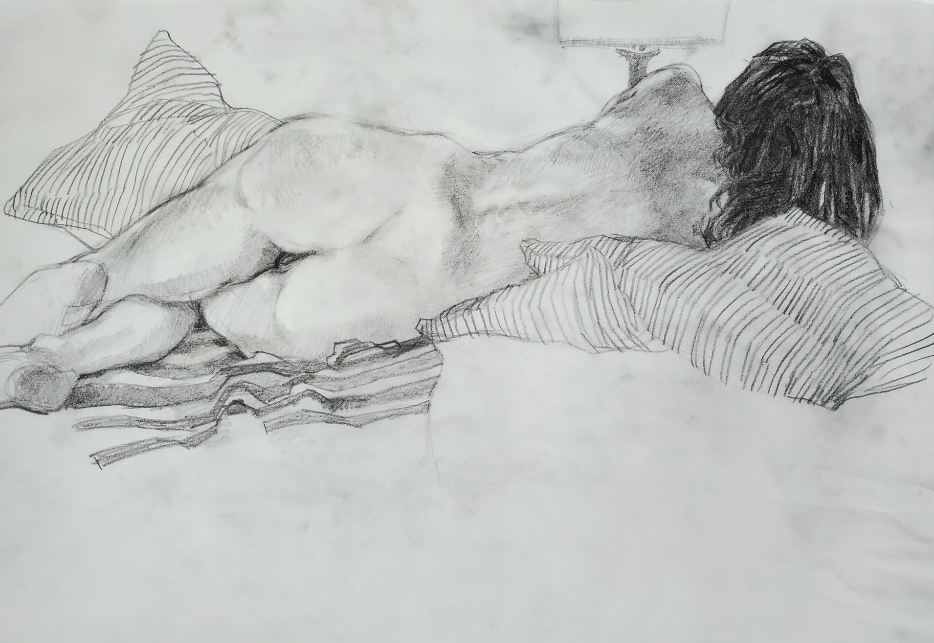 A pencil sketch of a woman lying on her stomach on a bed, facing away from the viewer, with striped pillows and patterned bedding.
