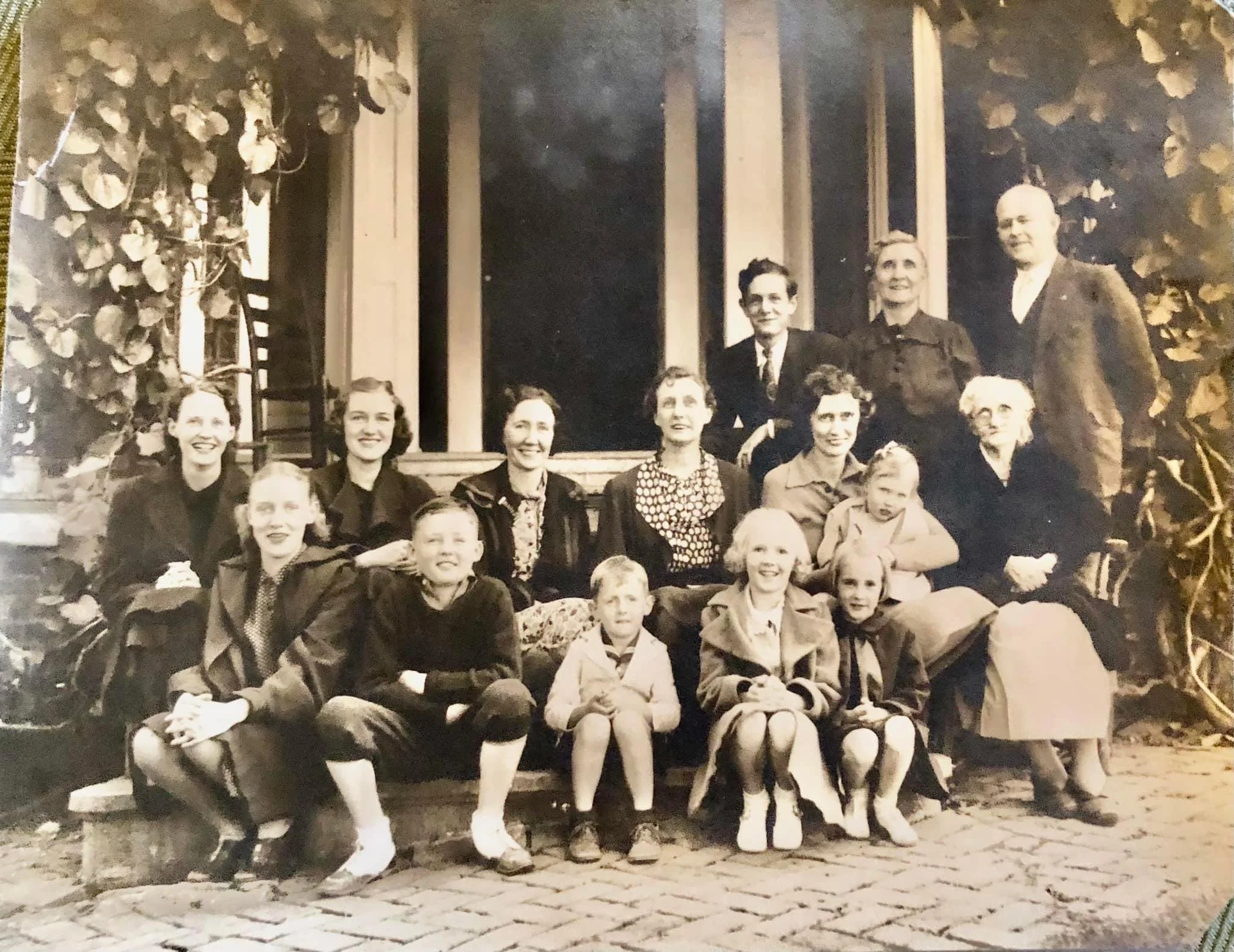 Monochrome family portrait with a group of people posed on brick steps in front of a house.