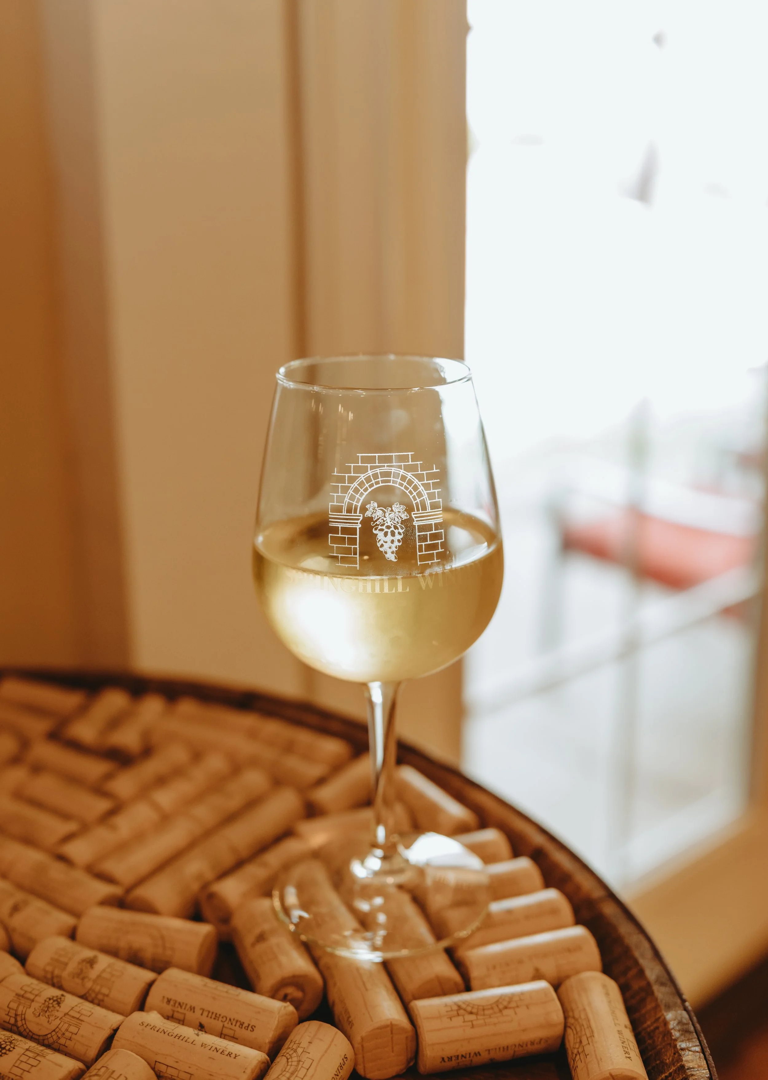 Glass of white wine sits on top of barrel covered with wine corks.