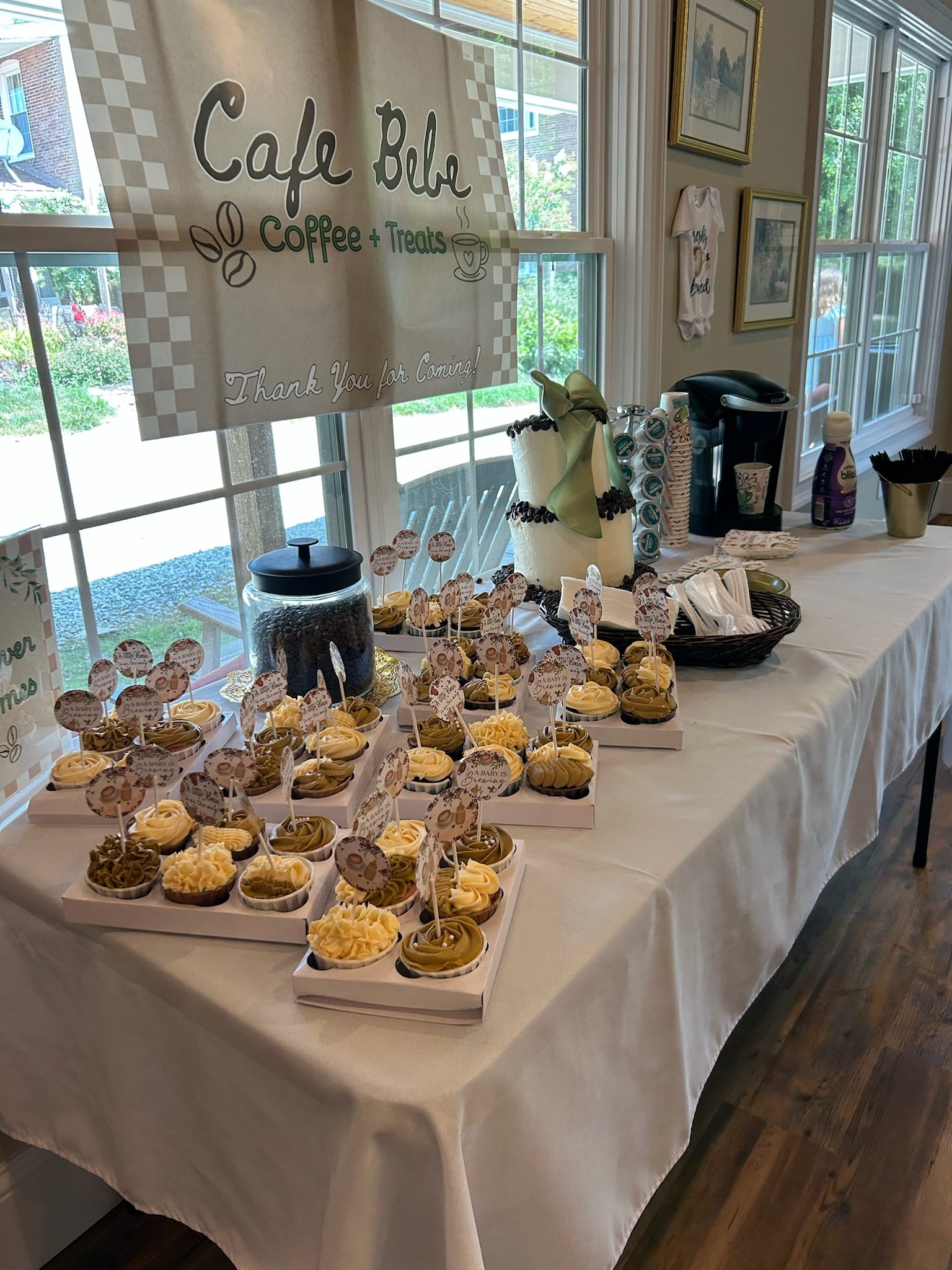 Coffee and treats table with cupcakes, a themed Café Bébé banner, and a full refreshment setup as part of a Springhill celebration experience.
