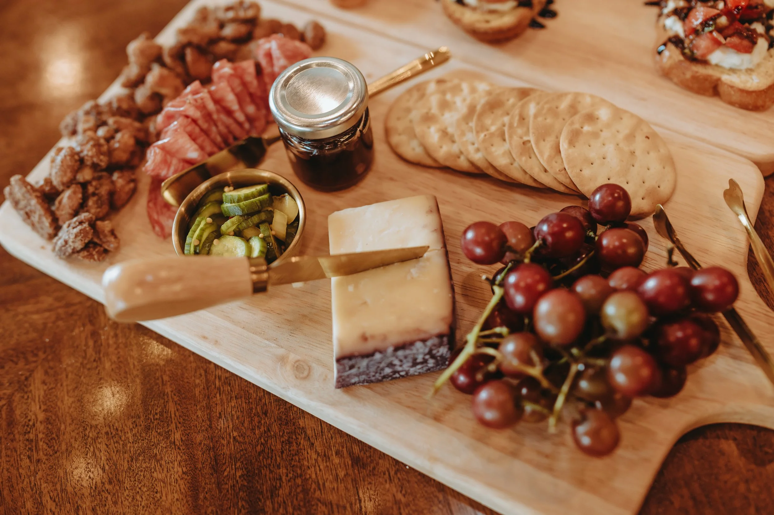 Charcuterie board with cheese, grapes, crackers, cured meat, jam, and pickled vegetables.