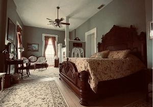 A bedroom with a large ornate wooden bed, a vanity table with a mirror, and a seating area with sofa and small table.