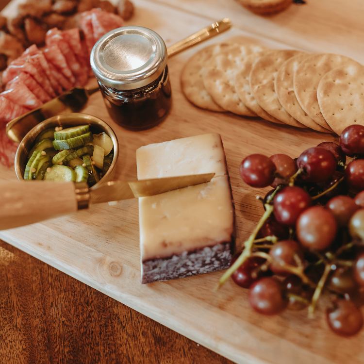 Charcuterie board with cheese, grapes, crackers, cured meat, jam, and pickled vegetables.