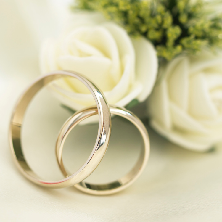 Gold wedding rings with white roses and greenery in a soft, romantic setting.