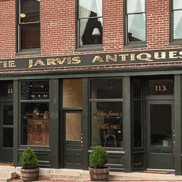Exterior of Nettie Jarvis Antiques in Bloomfield, Kentucky, featuring a brick storefront with gold-lettered signage and potted plants by the entrance.