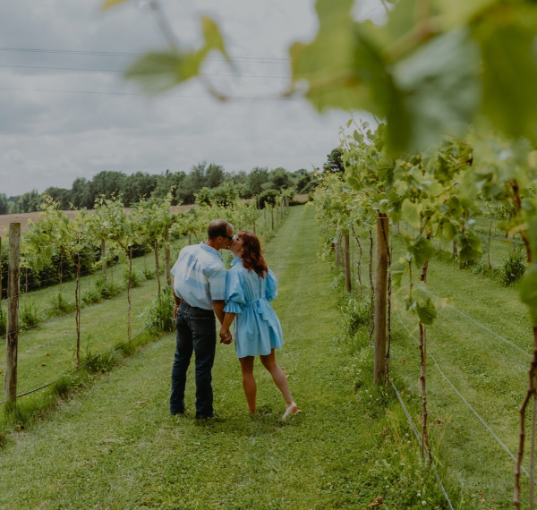 Couple sharing a kiss in the vineyard, holding wine glasses at Springhill Winery.