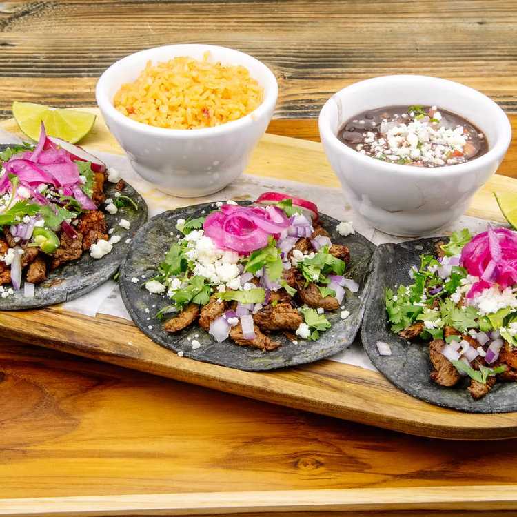 Blue‑corn tacos with seasoned meat, onions, cilantro, and cheese at Froggy’s Tex‑Mex in Bloomfield, Kentucky, served with rice, black beans, and lime wedges.