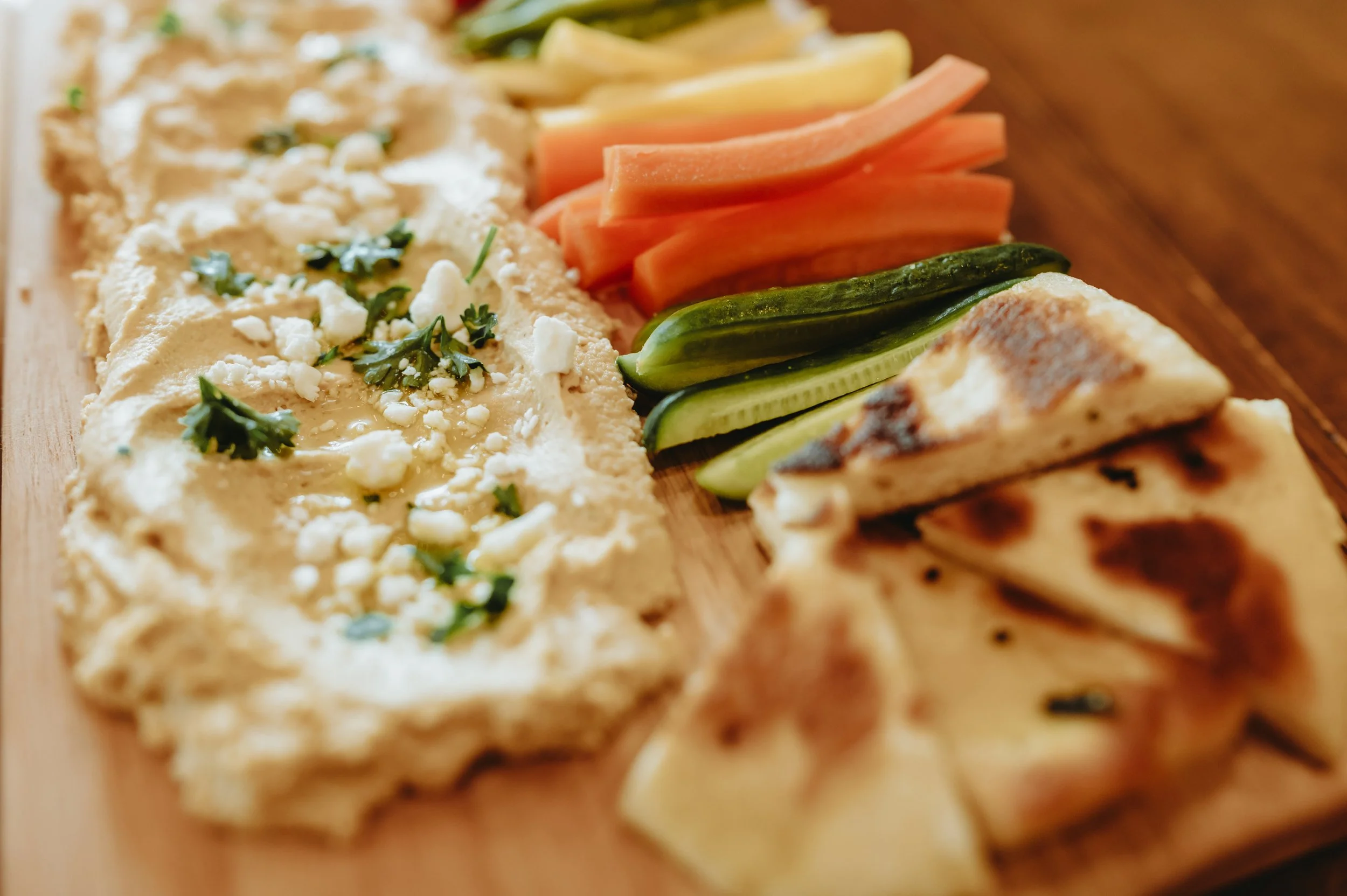 pita bread, carrots, zuchinni and other vegetables sliced thin sitting next to a thin layer of humus