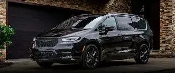 Black minivan parked in front of a brick and dark garage wall