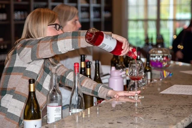 Pouring red wine during a Springhill tasting experience at the marble bar with bottles in the background.