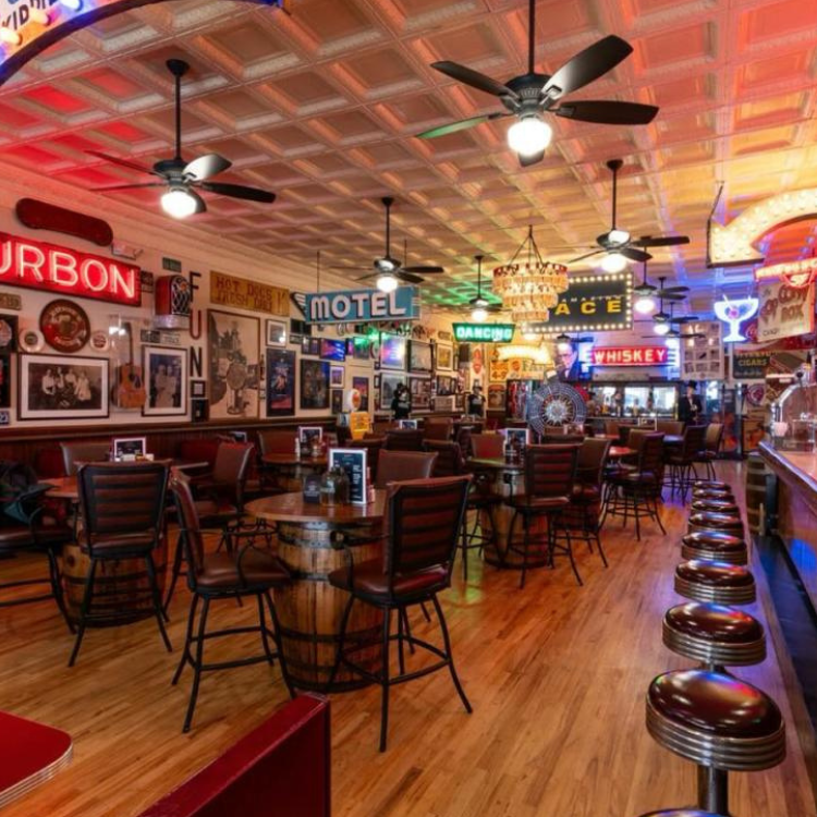 Retro interior of Earnie’s Tavern in Bloomfield, Kentucky, featuring neon signs, barrel tables, cushioned chairs, and a vintage bar counter.