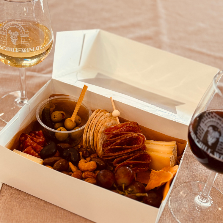Charcuterie box with meats, cheeses, fruit, and olives paired with red and white wine as part of the Springhill tasting experience.