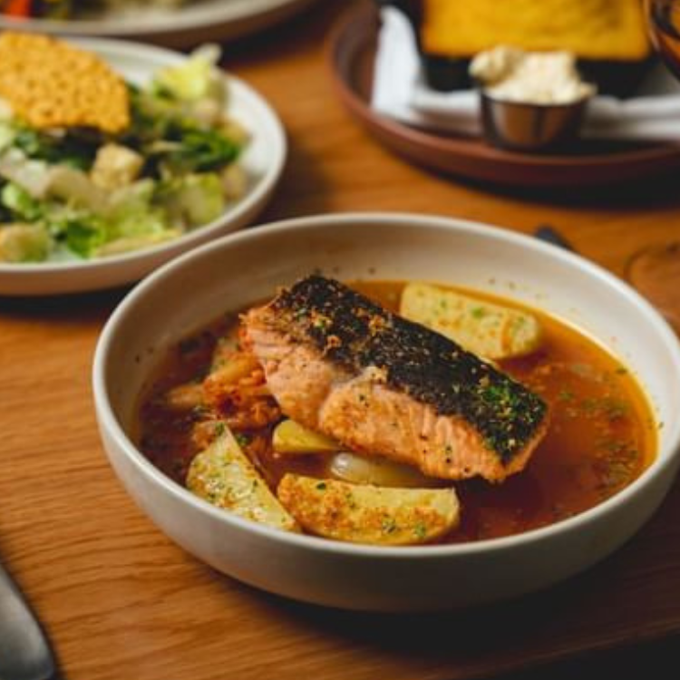 Salmon dish served in a rich broth at Toogie’s Table in Bardstown, Kentucky, with salad and bread in the background.