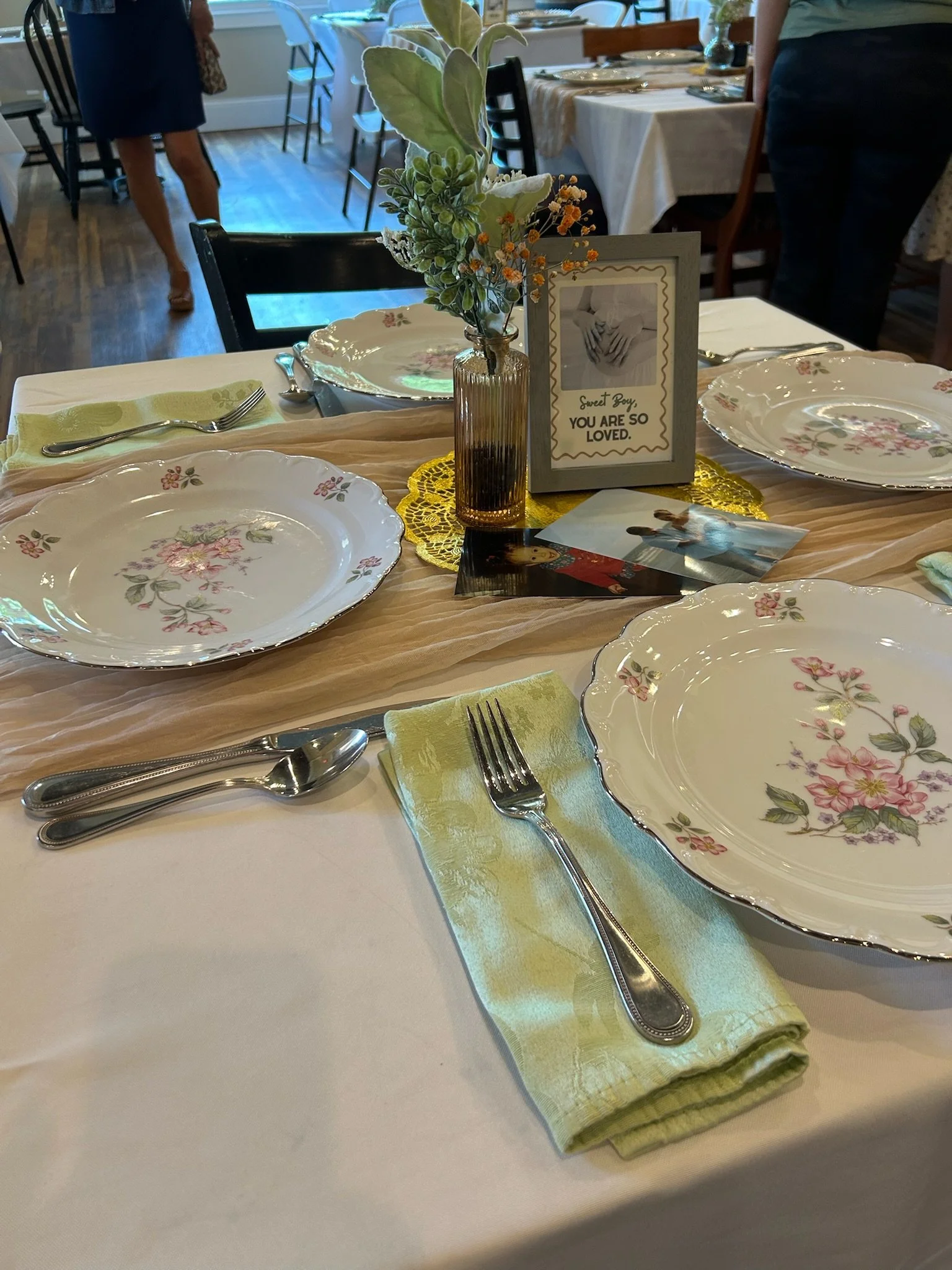 Warm table setting with floral plates, greenery, and a “Sweet Boy, You Are So Loved” sign as part of a Springhill celebration experience.