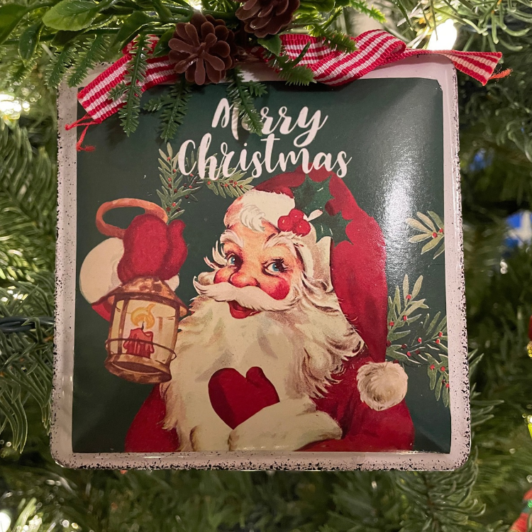 Vintage Santa Christmas ornament with holly, lantern, ribbon, and pine greenery.