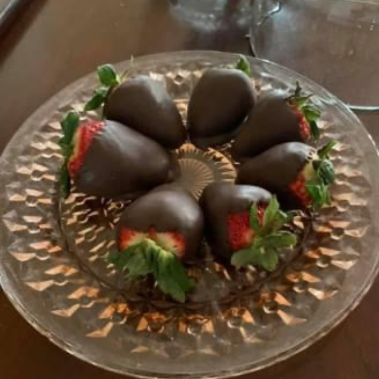 Glass plate with seven chocolate‑covered strawberries arranged in a circle on a wooden surface.