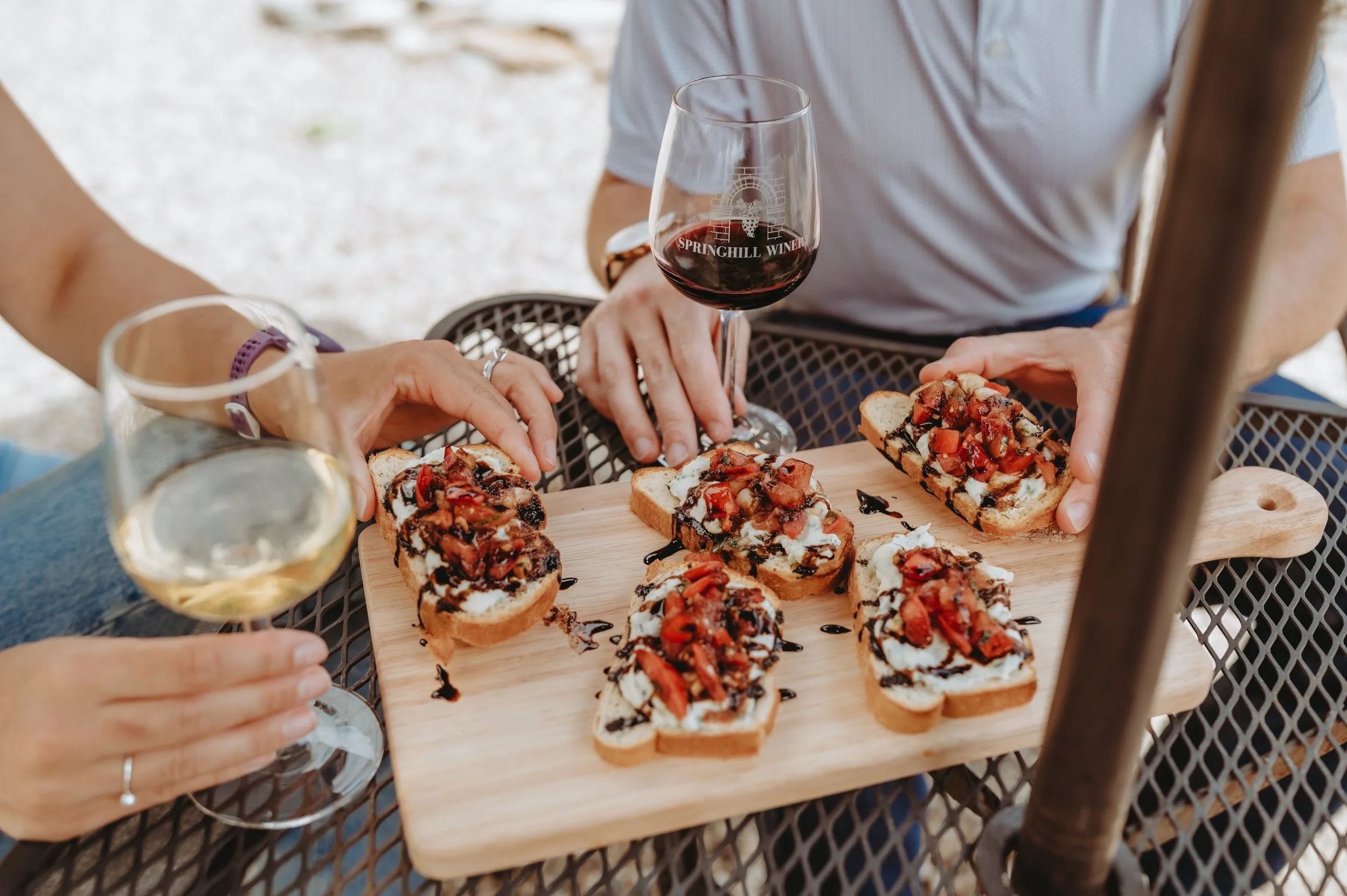 hands reach for bruschetta on a wooden board and wine filled glasses.