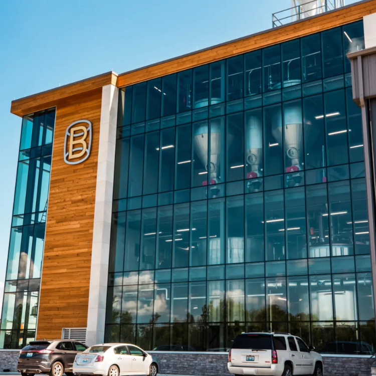 Cars sit in front of Bardstown Bourbon Company building with glass wall.