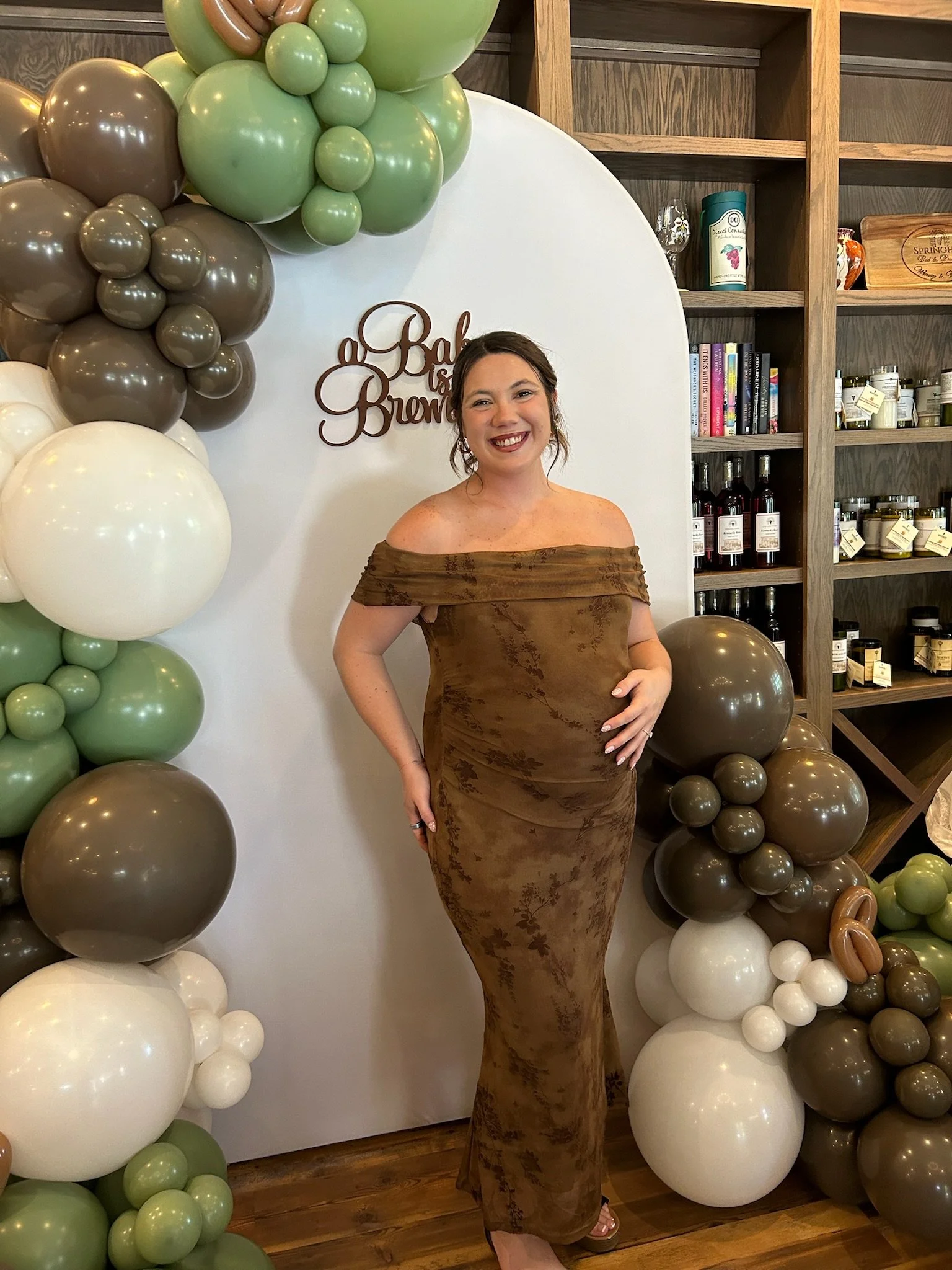 Guest standing in front of an “A Baby is Brewing” backdrop with balloon décor as part of a Springhill celebration experience.