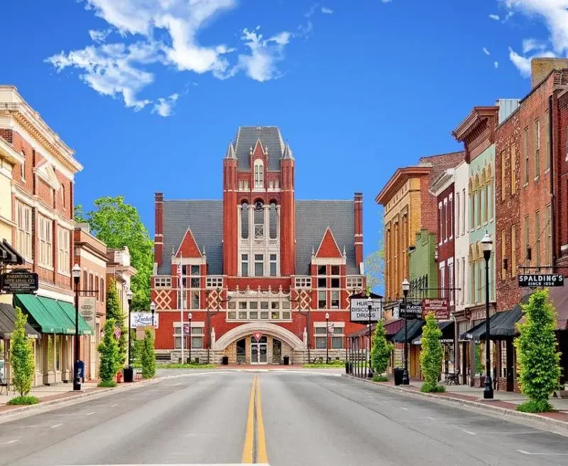 Historic Bardstown courthouse centered at the end of a brick‑lined downtown street, surrounded by storefronts, awnings, and a bright blue sky.
