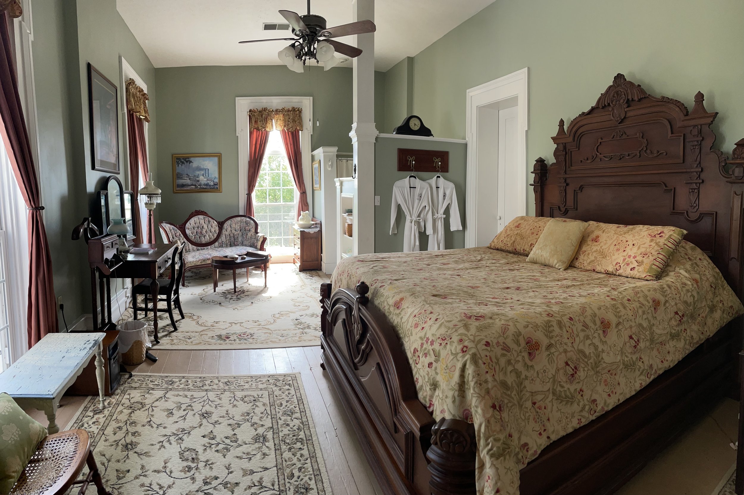 A spacious bedroom with a large ornate wood bed, a sitting area with antique furniture and a ceiling fan