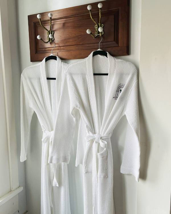 White robes hang from a piece of wood with hooks on a gray wall.