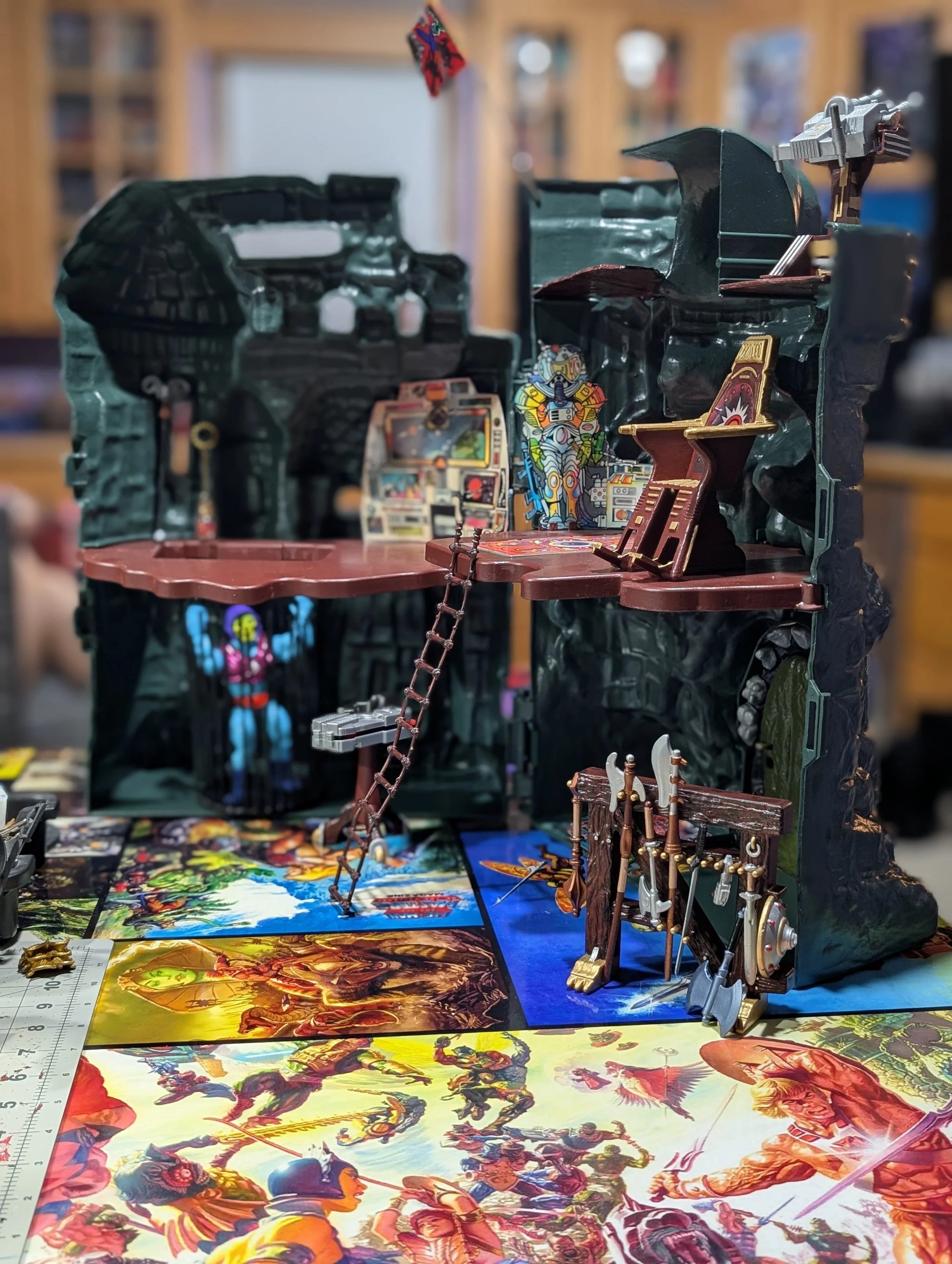 Assorted tabletop role-playing game miniatures, posters, and gaming materials on a table with a background of bookshelves.