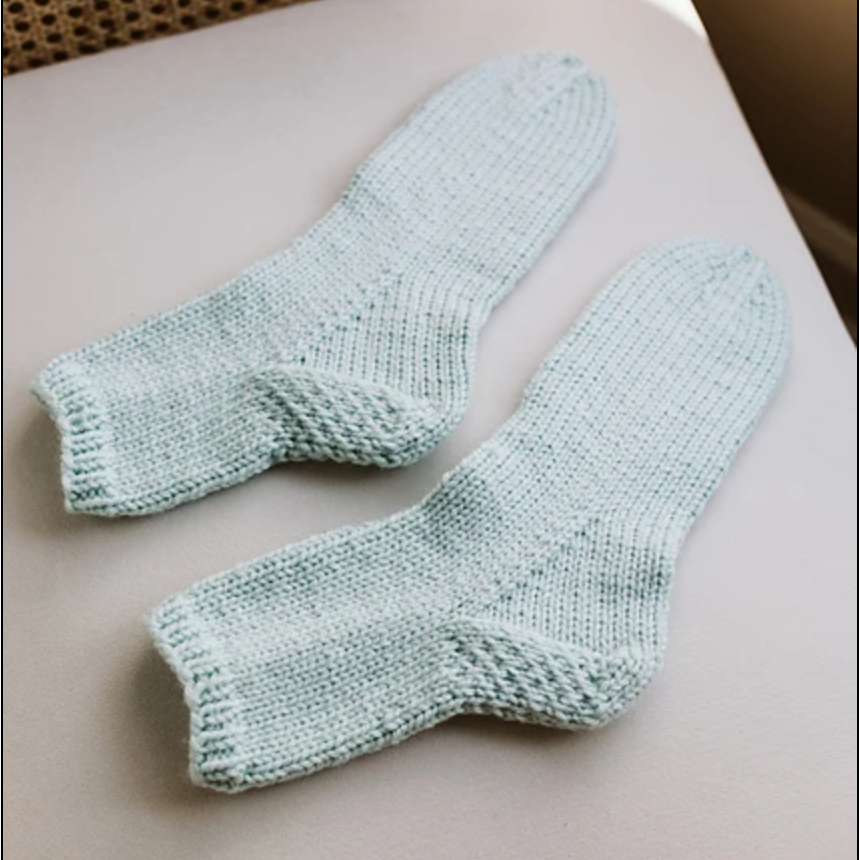 A pair of light blue worsted weight socks on a chair. They're all-over stockinette stitch with an eye of partridge heel flap and gusset.