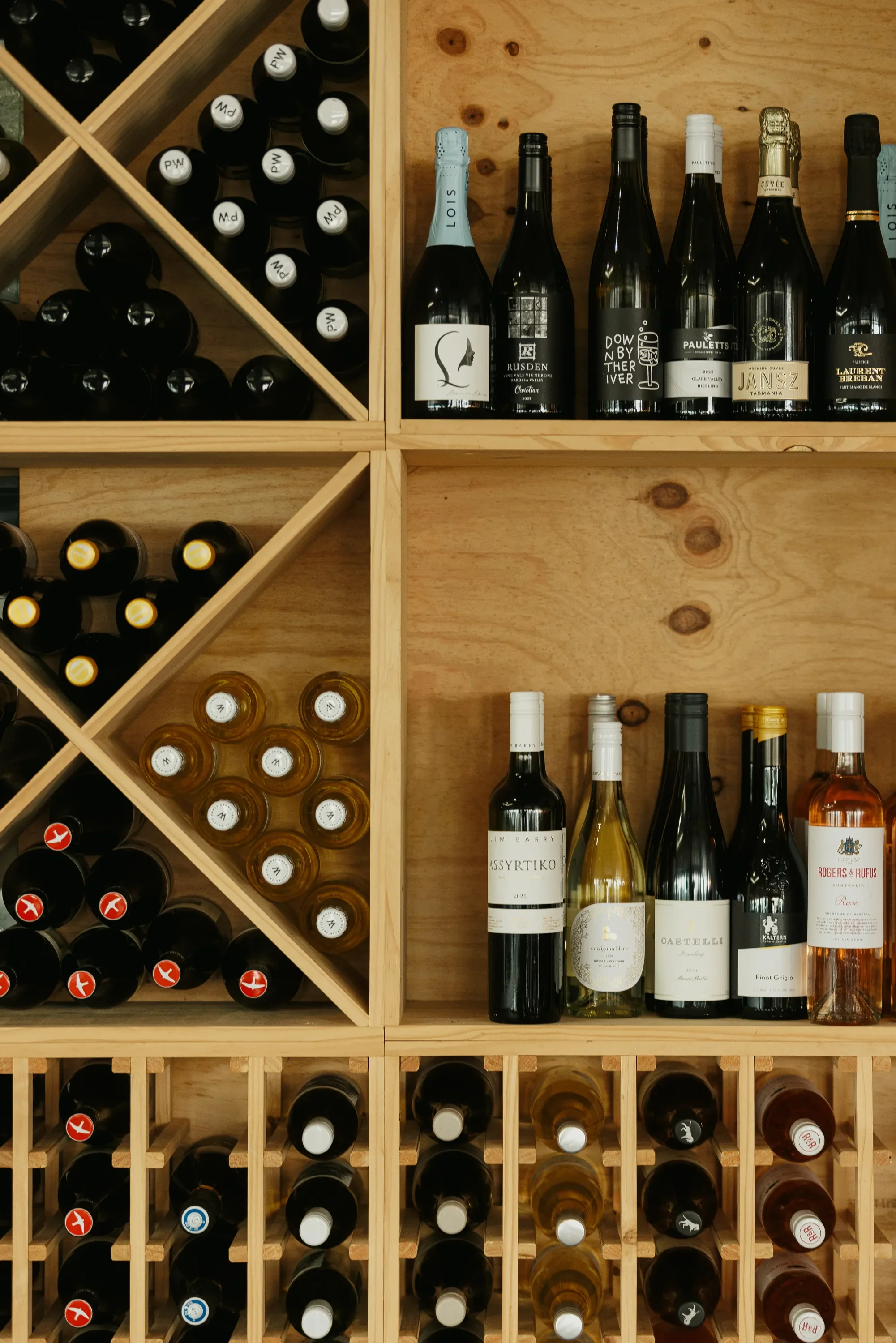 A wooden wine rack holding multiple bottles of wine, organized in cubby holes and wine bottle slots, including white, red, and sparkling wines.