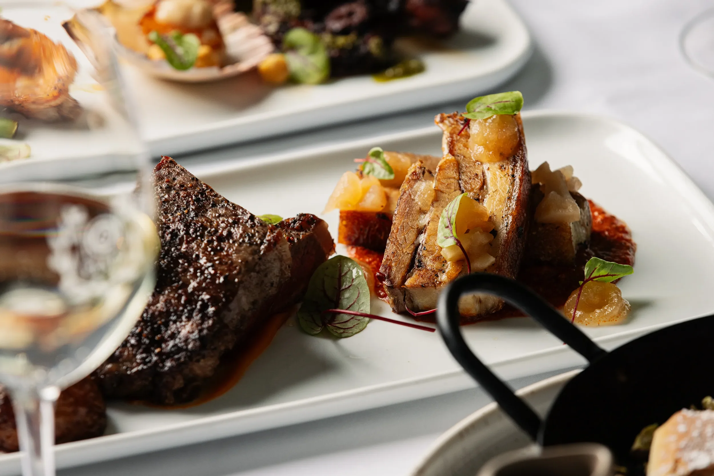 Close-up of prepared gourmet seafood dishes on a white serving tray, featuring items like scallops and fish with garnishes, accompanied by microgreens.