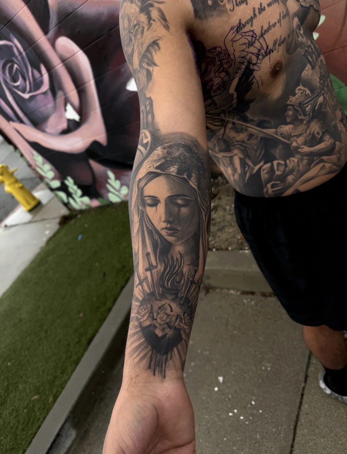 Tattoo of a woman with closed eyes, with a heart with roses and flames below, on an arm.