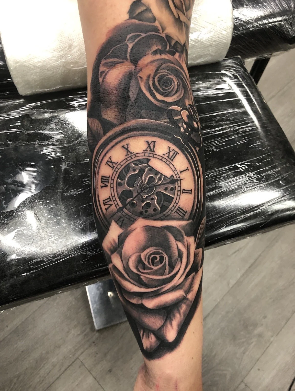 Tattoo of a pocket watch and roses on a person's arm.