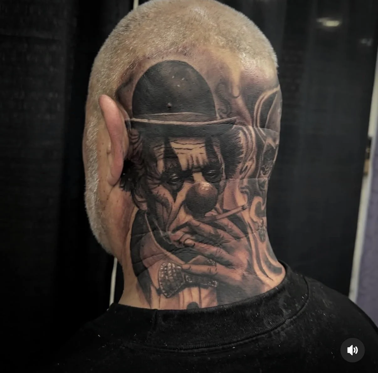 Tattoo of a clown with a hat, holding a cigarette, covering part of the face at the back of a person's head.