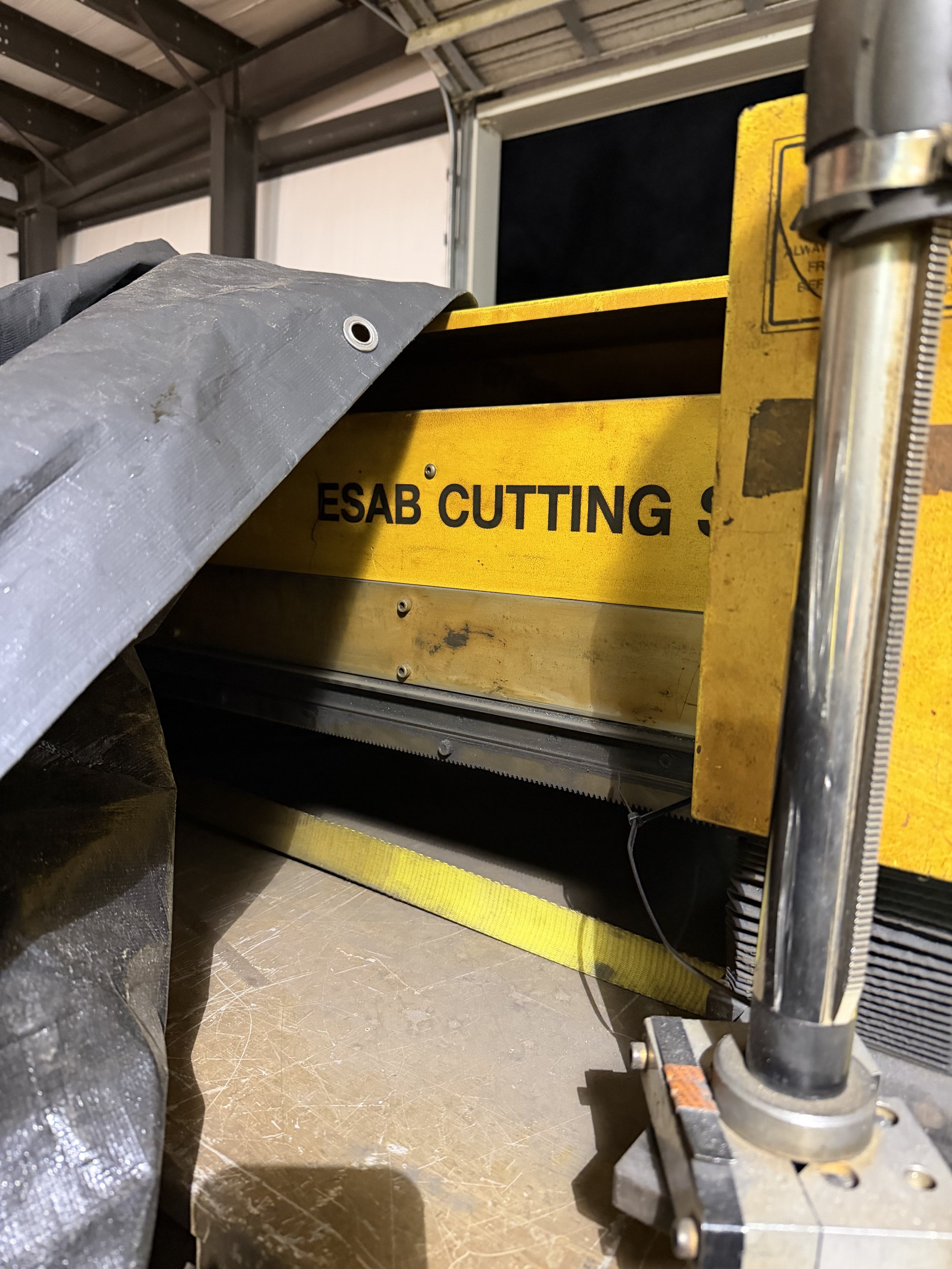 Industrial workshop scene with machinery, a partially visible circular saw, and a yellow safety barrier with the words "ESAB Cutting".