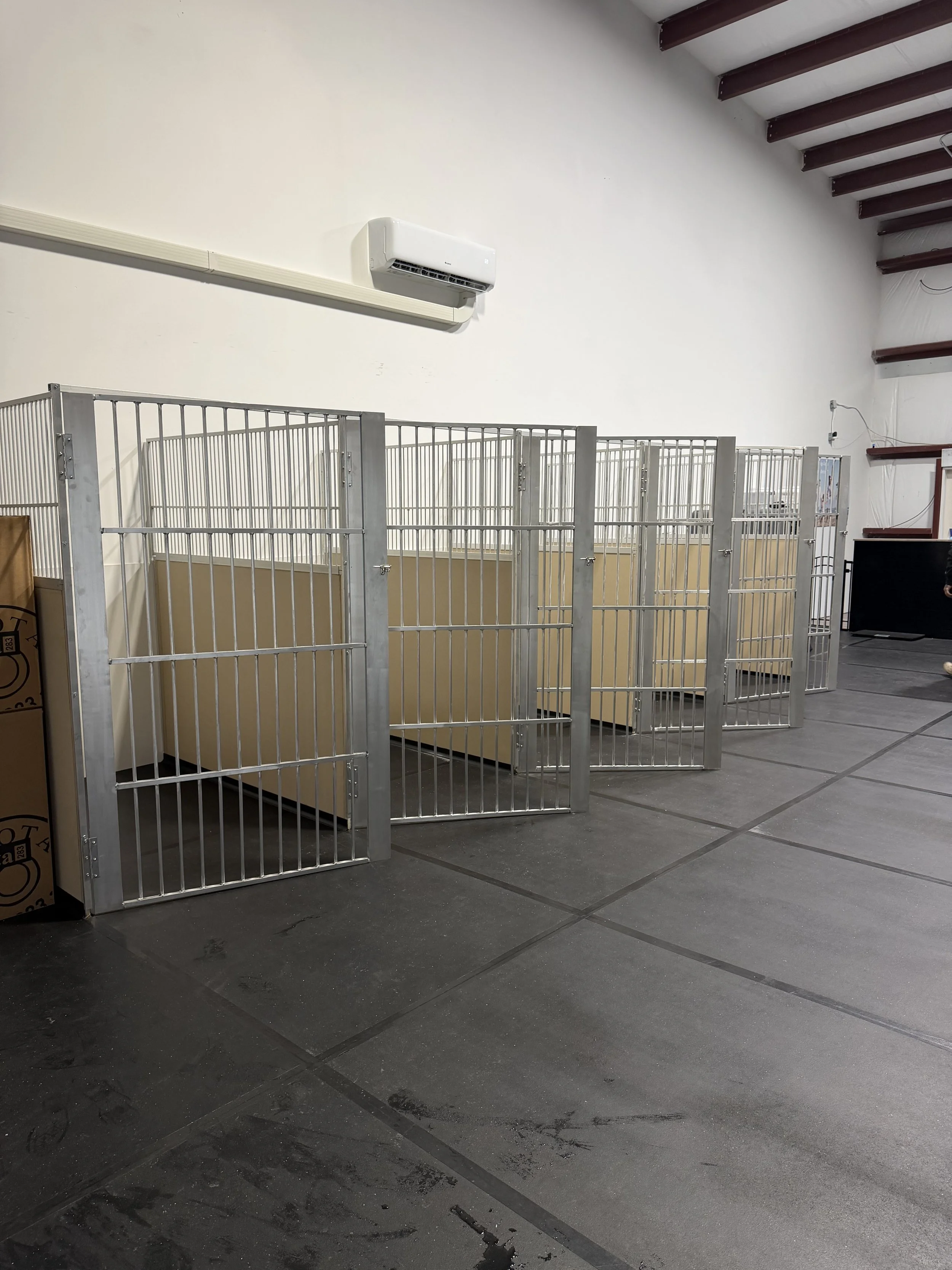 Indoor facility with metal cages, a white wall, an air conditioning unit, and a staircase with red steps.