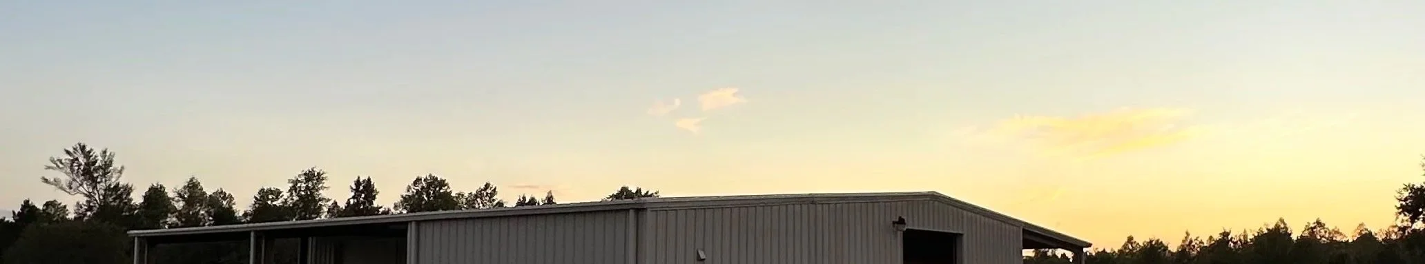 A metal building with trees in the background during sunset.