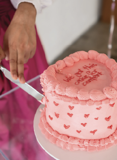 Person slicing a pink birthday cake decorated with small hearts and whipped border, with message 'Let me slice my cake' written on top.