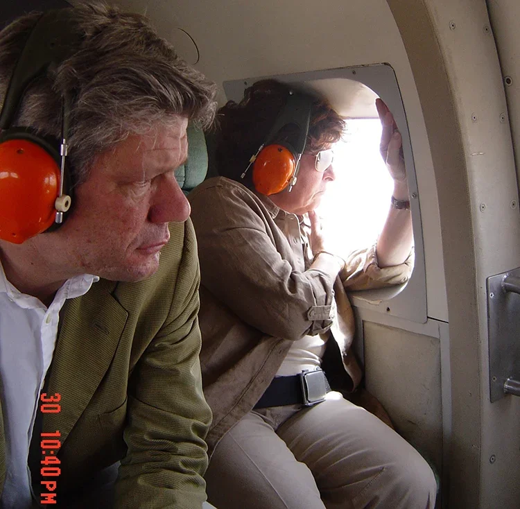 Two people wearing orange headphones sit inside an aircraft, looking out the window.