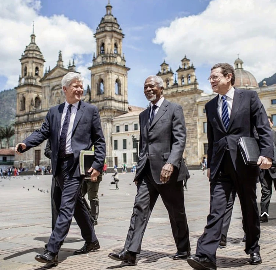 Three men in suits walking and talking in a plaza with a historic church in the background.