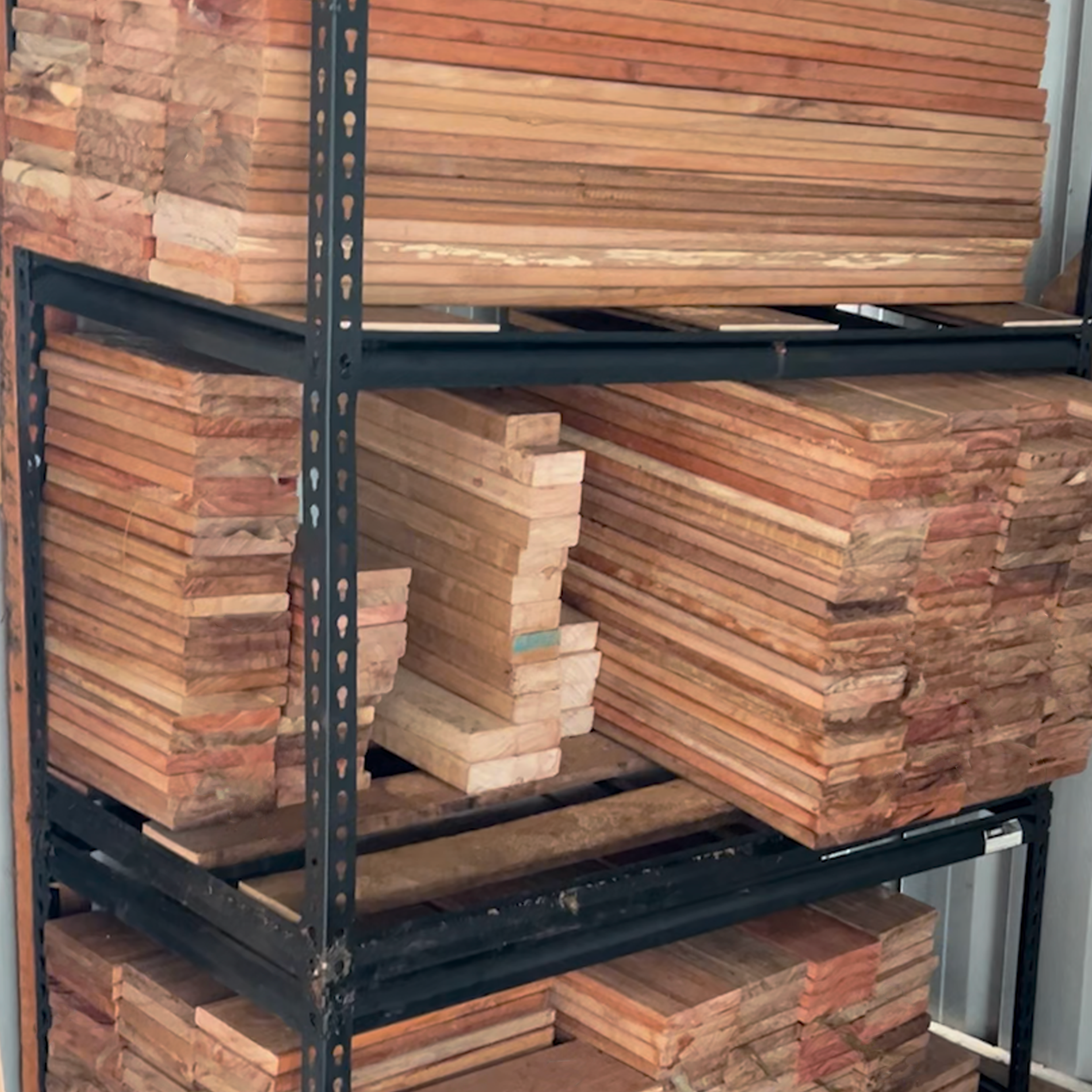 Stacked wooden planks on metal shelving in a storage area.