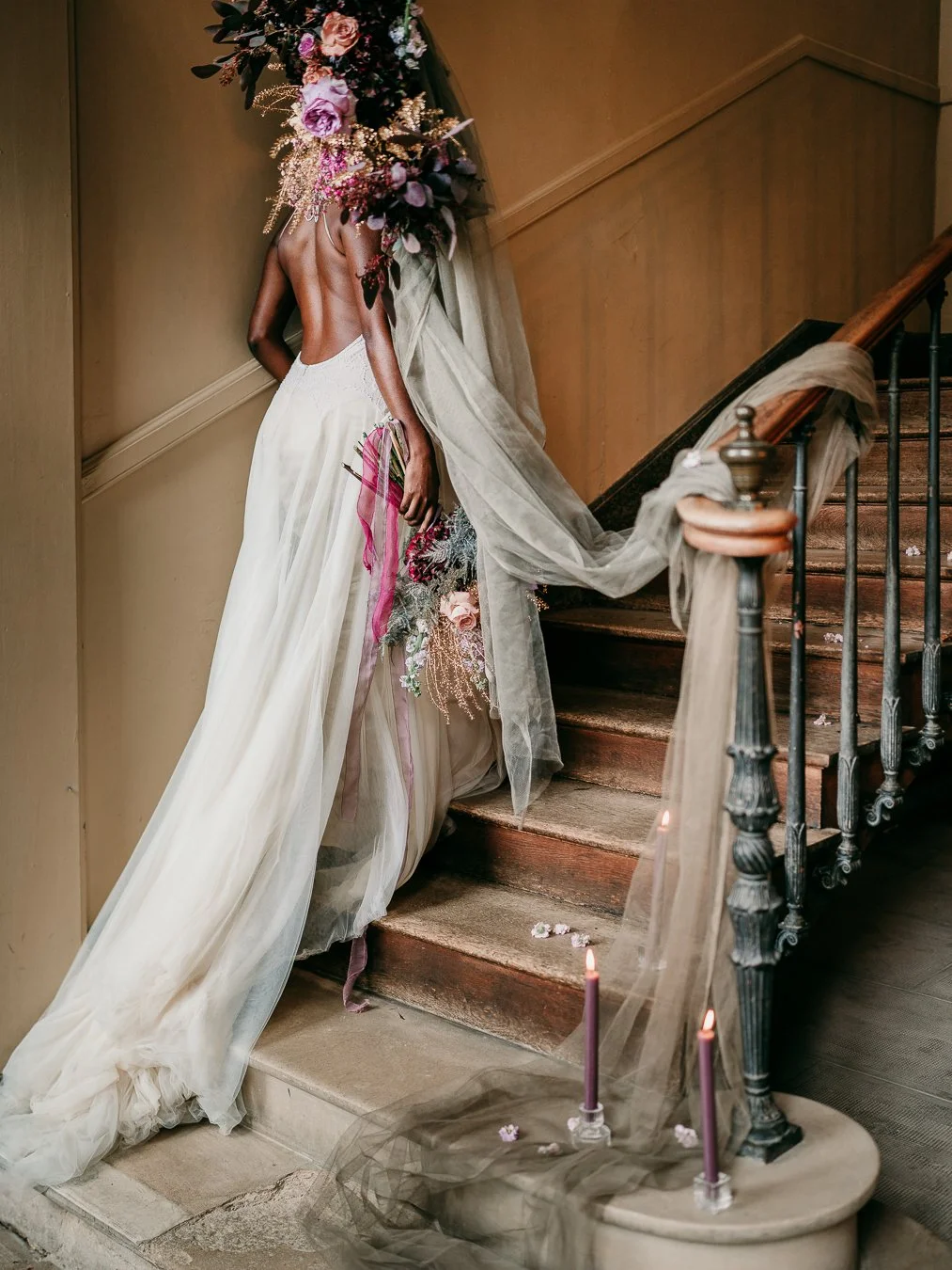 Editorial wedding photography by Weddings by Qay — bride descending vintage staircase with cascading bouquet, candles, and tulle veil