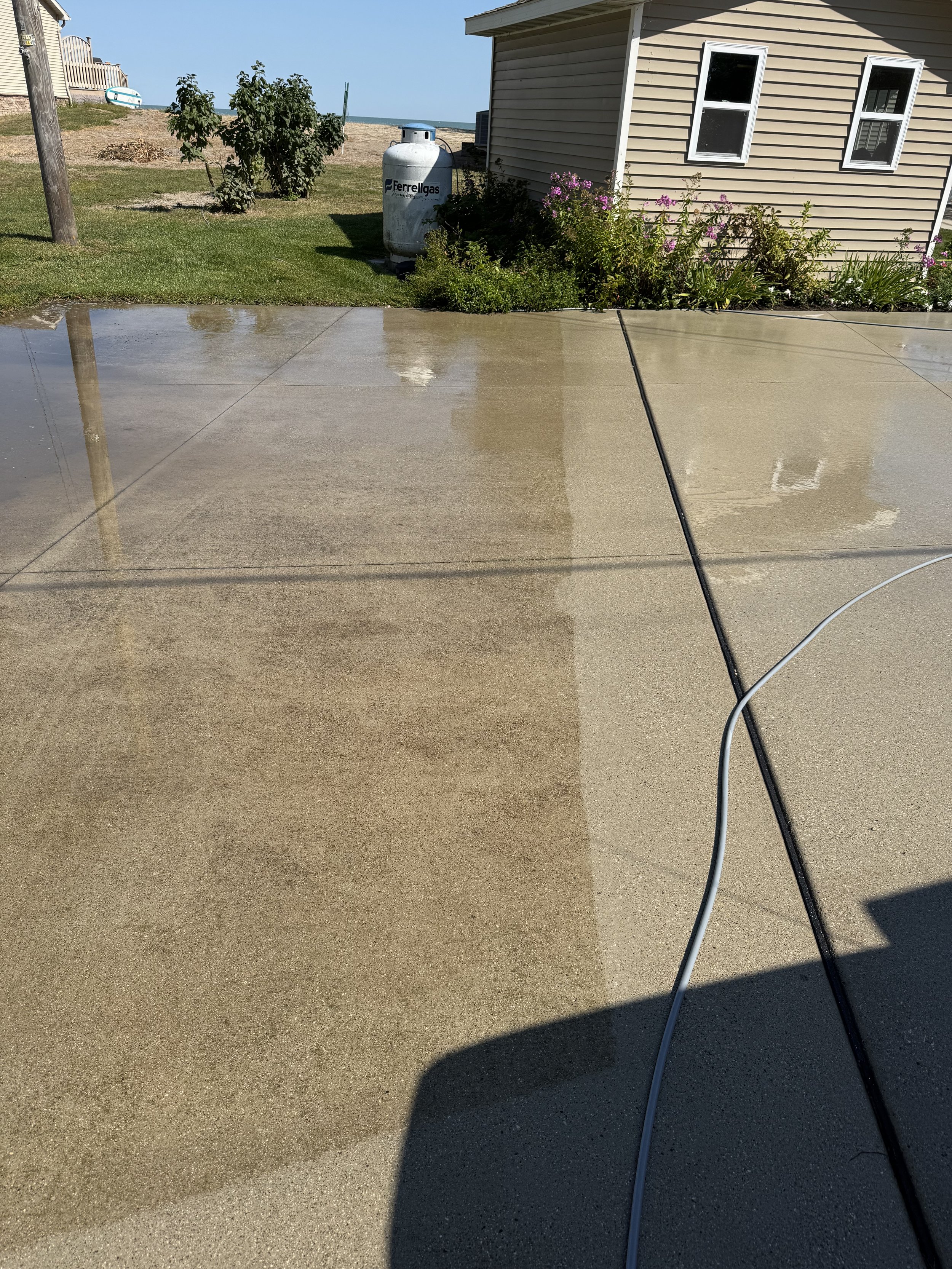 Photo showing a wet concrete patio with a garden and house in the background, and a propane tank labeled 'Ferrelgas' near the house.