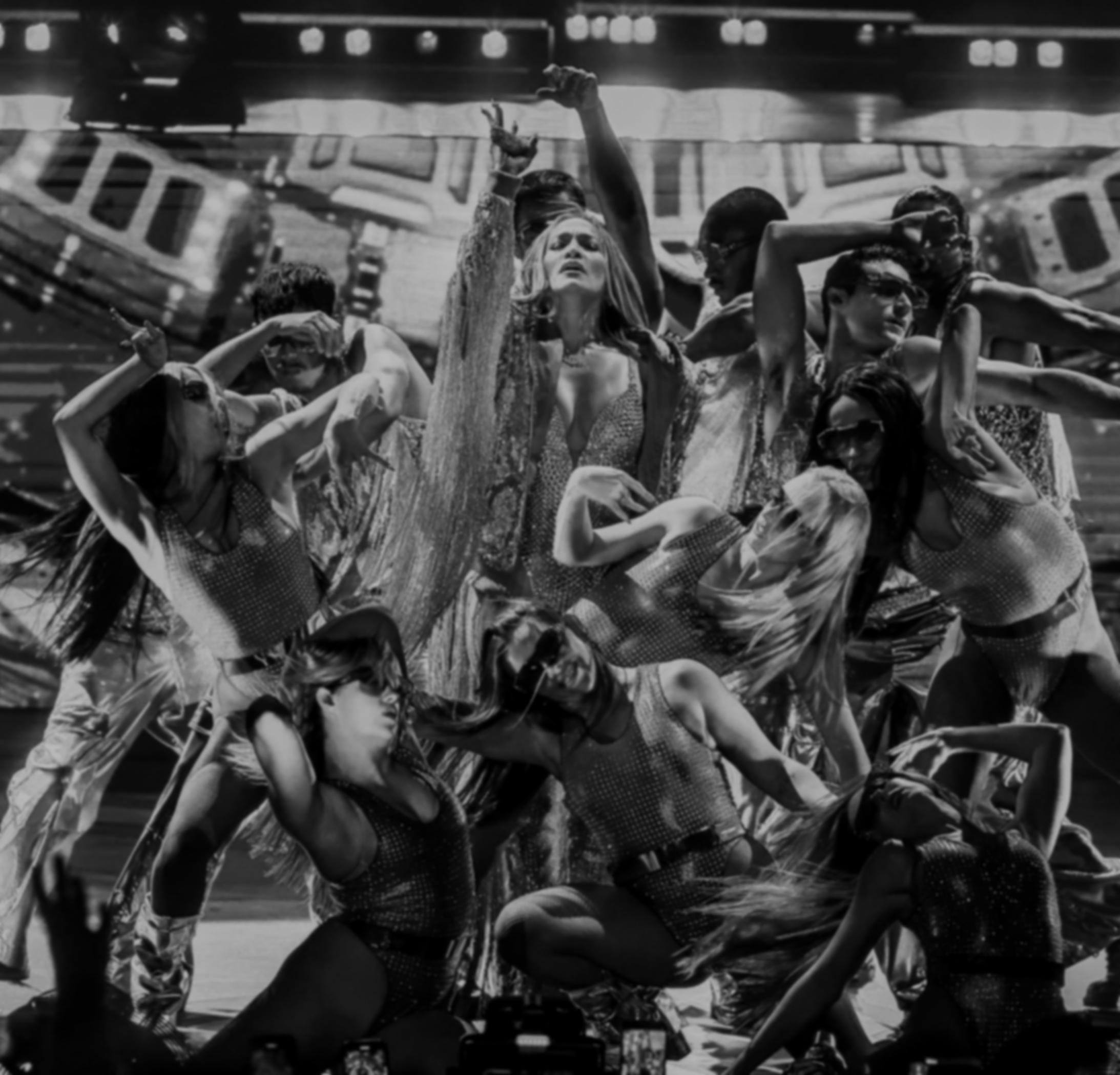 People riding bikes in a group, with a woman in the center raising one hand and looking upward, all under a structure with lights.