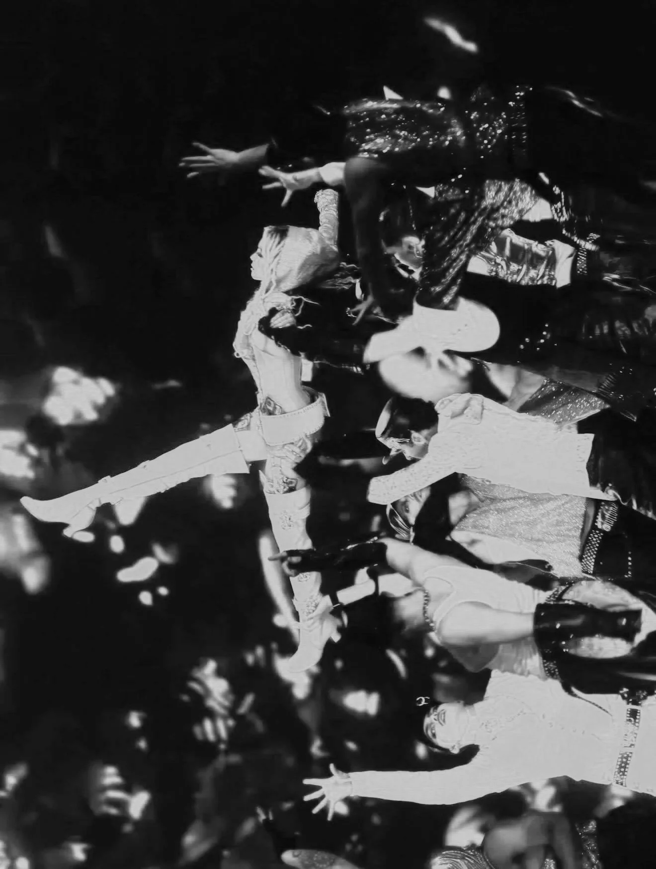 Black and white photo of a group of people, some dancing or performing, with leaves in the foreground.