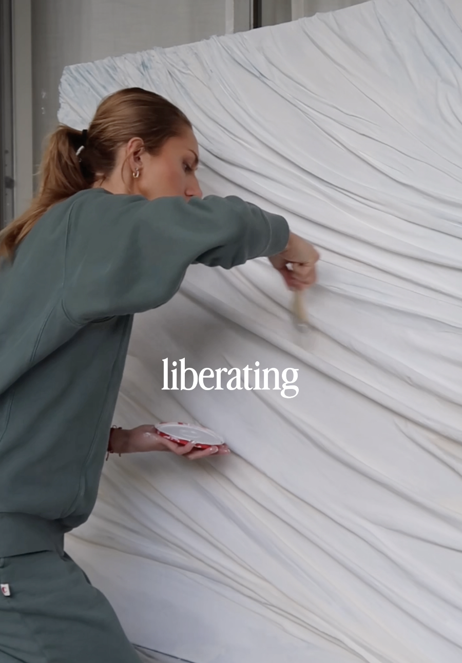 Woman painting white fabric to cover a large surface, with the word 'liberating' overlaid.