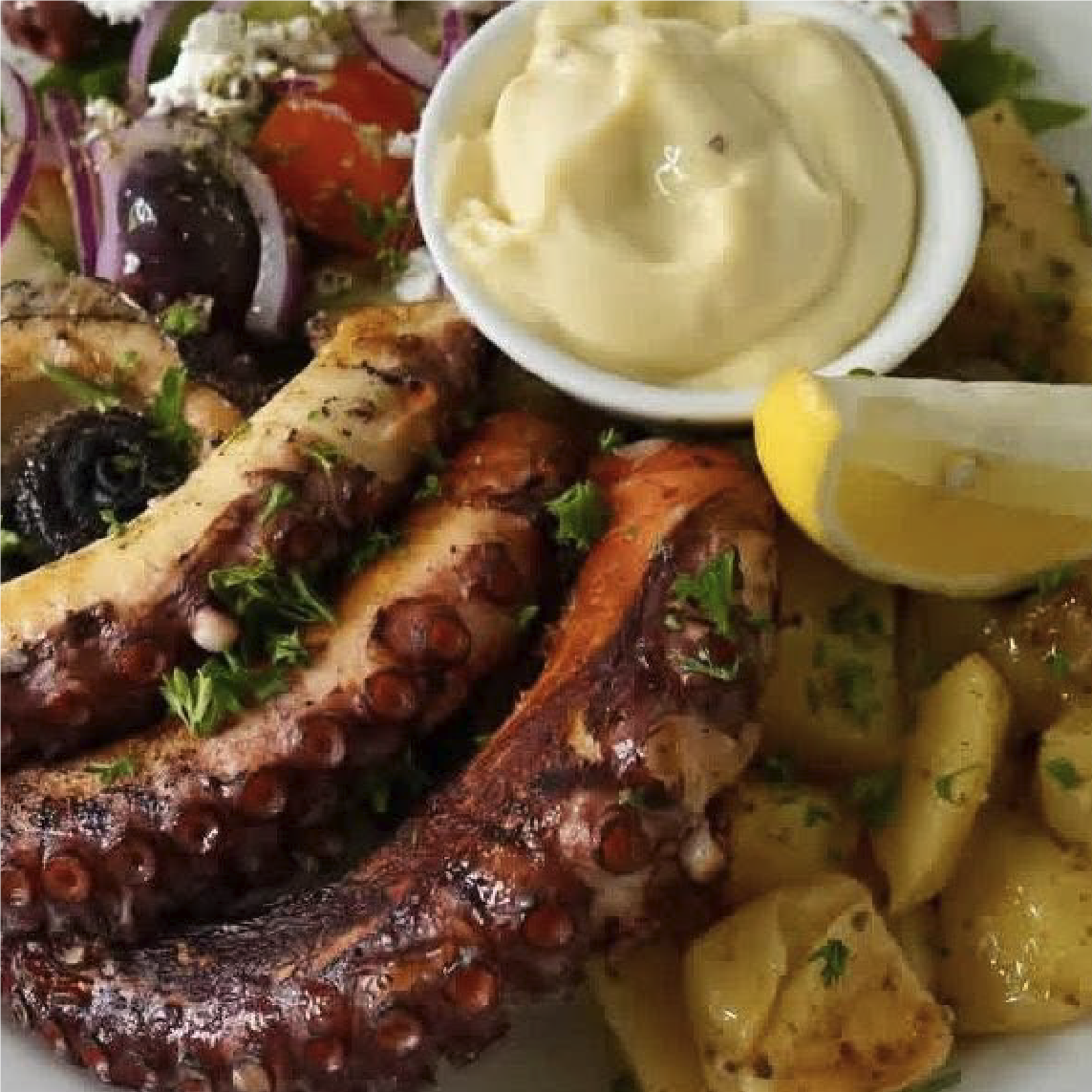 Greek grilled octopus tentacles with parsley, served with lemon wedges, potatoes, and a side of creamy dipping sauce.