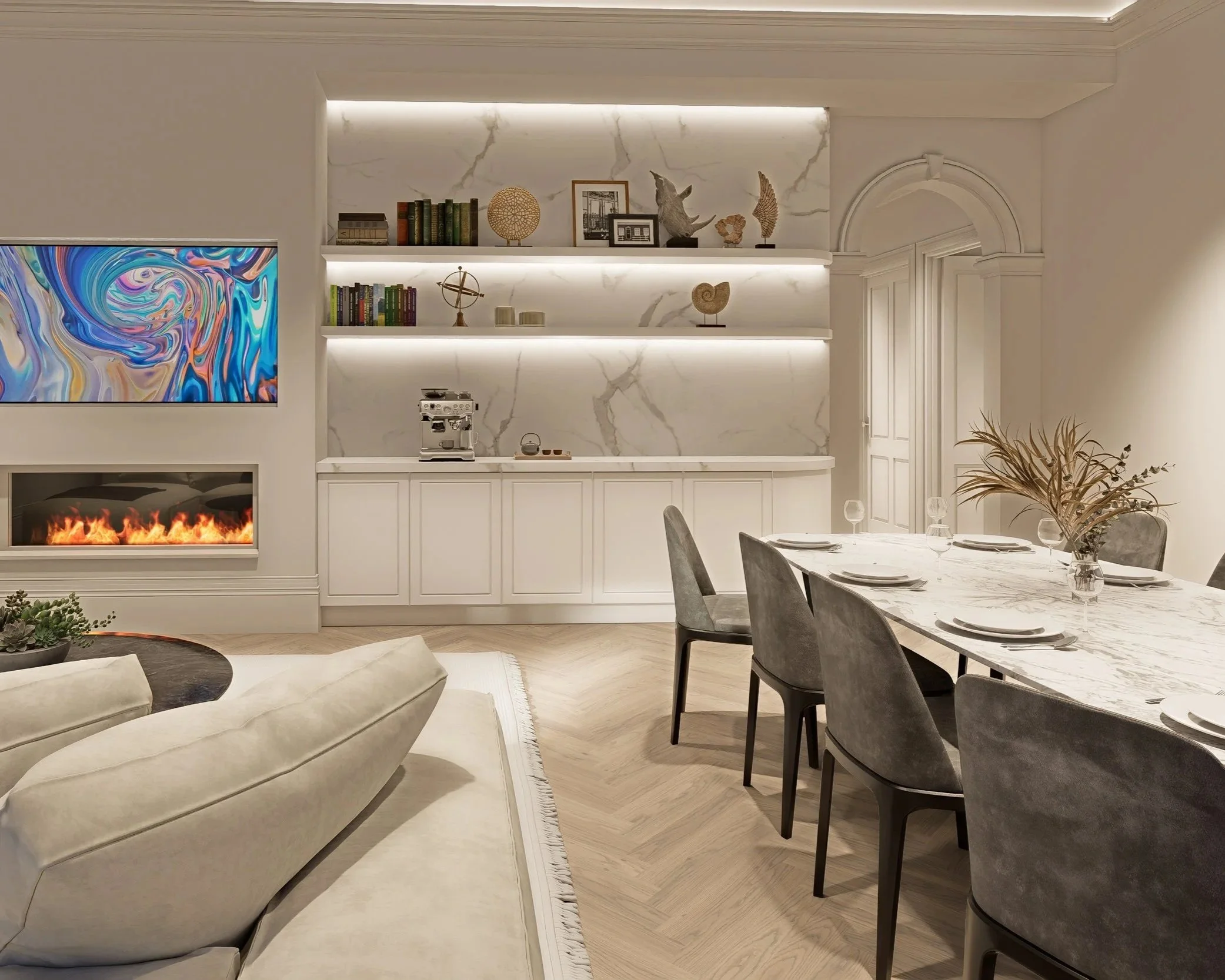 A modern living room and dining area with white marble walls and cabinetry, equipped with a coffee machine, a television displaying an abstract colorful design, and decorative objects on shelves including books, sculptures, and framed photos.