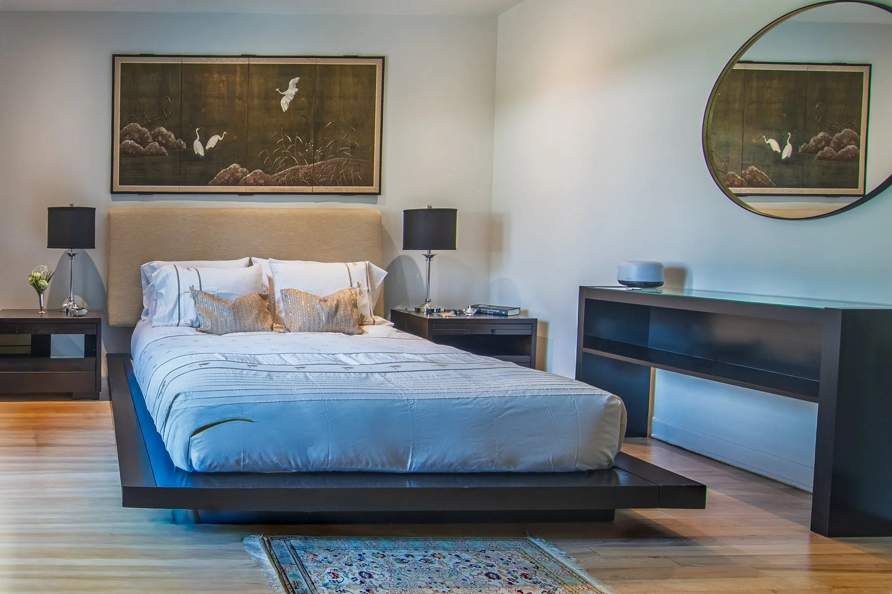 Bedroom with a low platform bed, a gilded folding screen above the headboard, and a round mirror reflecting it