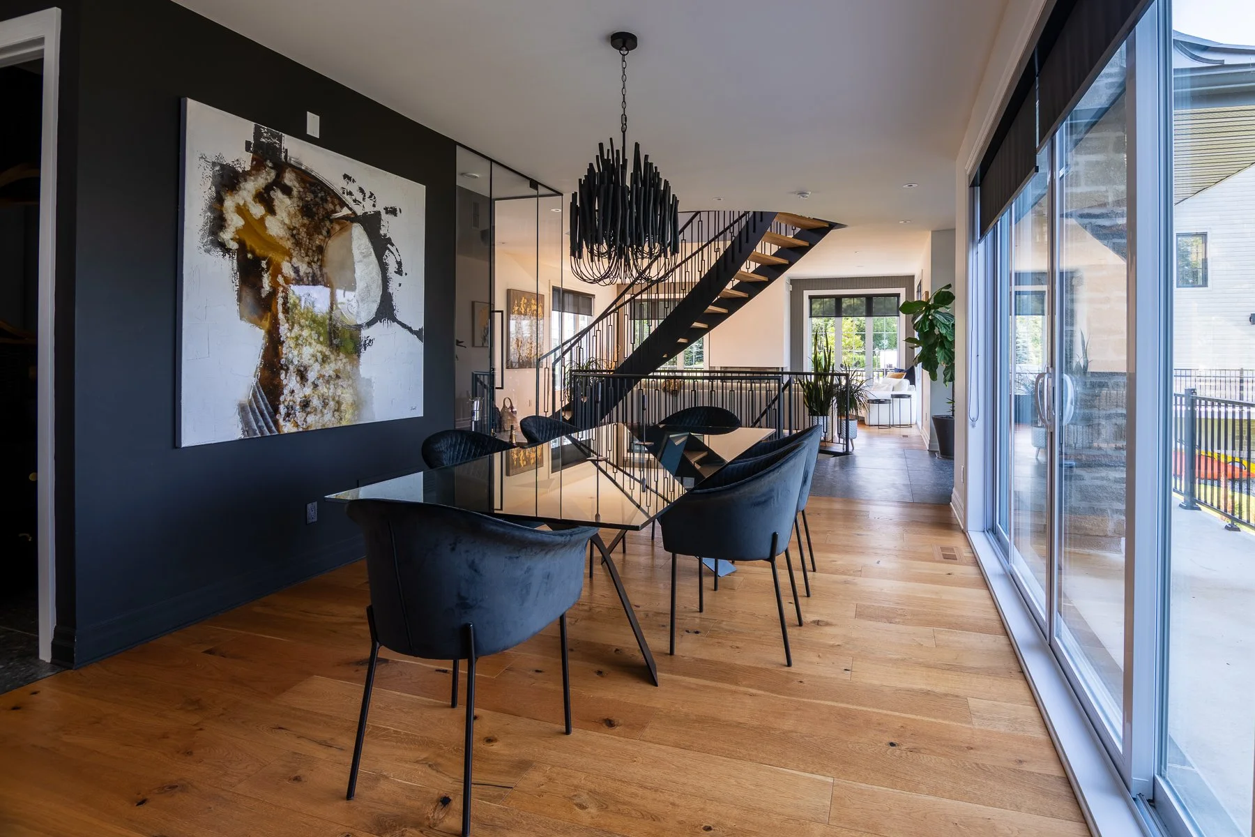 Dining room with a black feature wall, a large abstract canvas, and a glass table set beneath a sculptural black chandelier